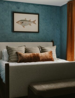 Slaapkamer met een lichtblauwe muur, houten nachtkastje en linnen beddengoed
