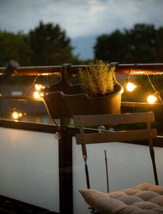 Een klein balkon met lichtsnoer, kussens en een plaid in de avond
