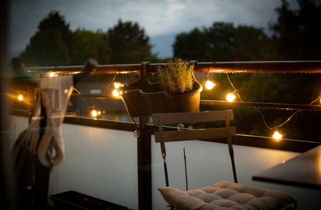 Een klein balkon met lichtsnoer, kussens en een plaid in de avond