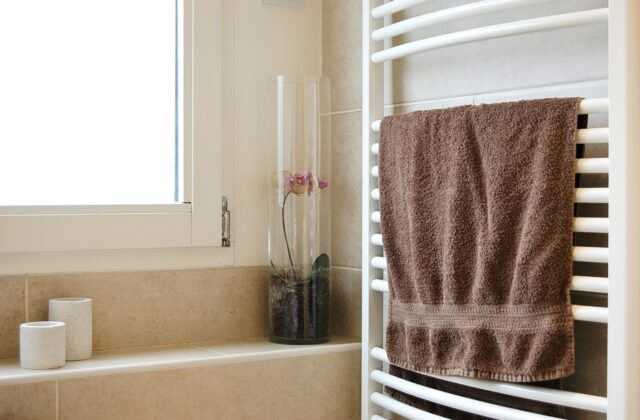Witte handdoekradiator met opgevouwen handdoeken in een lichte badkamer met tegels