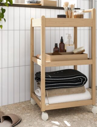 Bamboe roltafel met handdoeken, flesjes en bakjes tegen een witte tegelwand in een badkamer