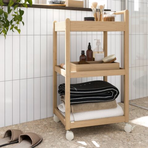 Bamboe roltafel met handdoeken, flesjes en bakjes tegen een witte tegelwand in een badkamer