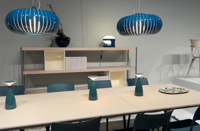 Stand met eettafel, blauwe hanglampen en open kast op Salone del Mobile in Milaan