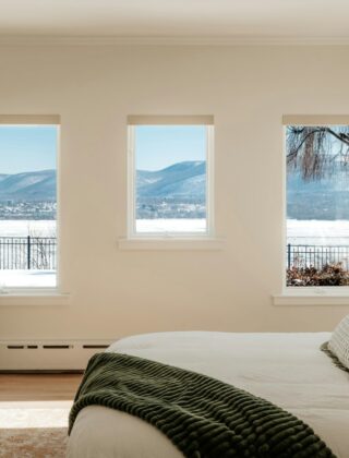 Opgemaakt bed met een dik wit dekbed en een wollen plaid in een lichte slaapkamer