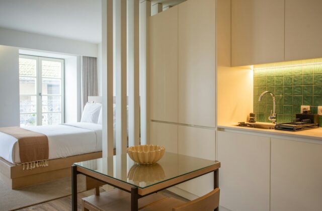 Lichte studio met een opgemaakt bed achter een open kast en een zithoek ervoor